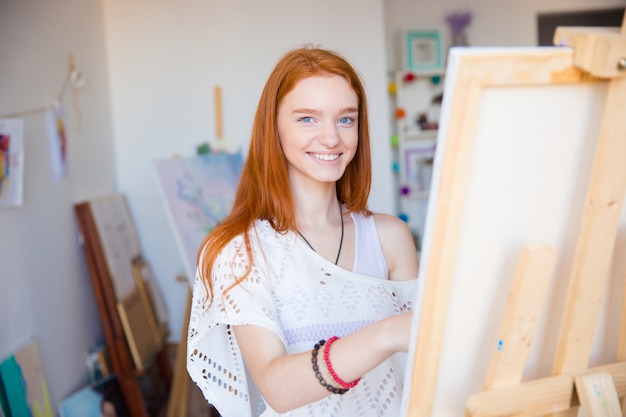 Alegre e atraente jovem artista pintando sobre tela em