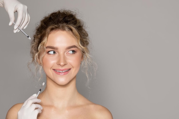 Foto alegre e bela dama recebendo injeções faciais em pé sobre um fundo cinza olhando de graça