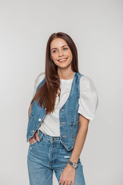 Alegre e bonita jovem estilosa com um sorriso em roupas jeans da moda em um fundo branco no estúdio