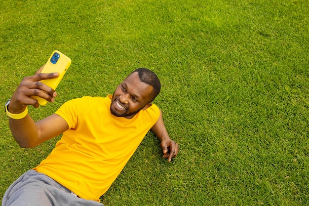 Alegre e bonito homem afro-americano deitado na grama relaxando e fazendo uma pausa após o trabalho esportivo