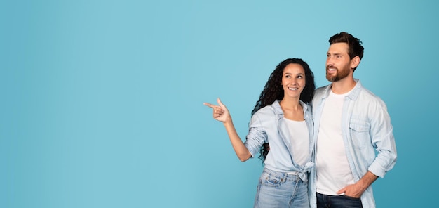 Alegre e bonito jovem europeu e senhora árabe em abraço casual e apontar o dedo para o espaço vazio