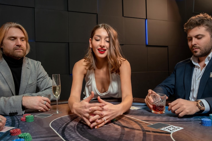 Foto alegre e elegante garota de cabelos castanhos quebrando o banco no jogo de pôquer, juntando fichas ganhas enquanto está sentado na mesa de jogo entre jogadores masculinos frustrados. conceito de jogo de boa sorte