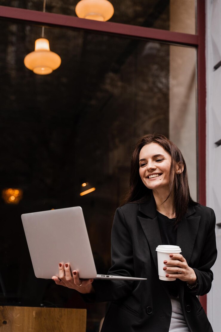 Alegre e emocional jovem está trabalhando on-line no laptop e sentada no terraço de verão no café Garota feliz e animada com uma xícara de café e laptop está curtindo seu estilo de vida fora do café