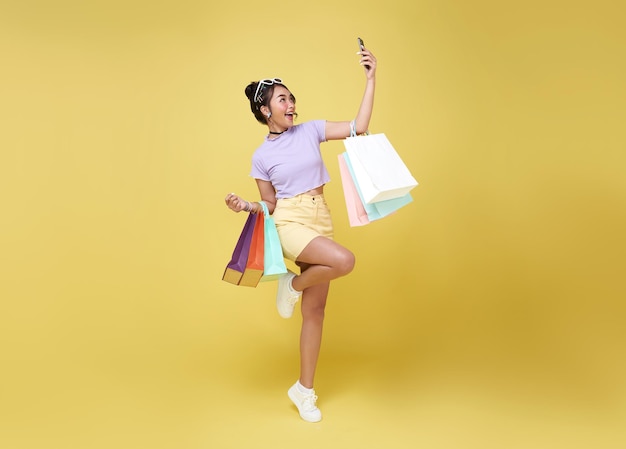 Alegre e feliz mulher asiática gostando de fazer compras, ela está carregando sacolas de compras e smartphone