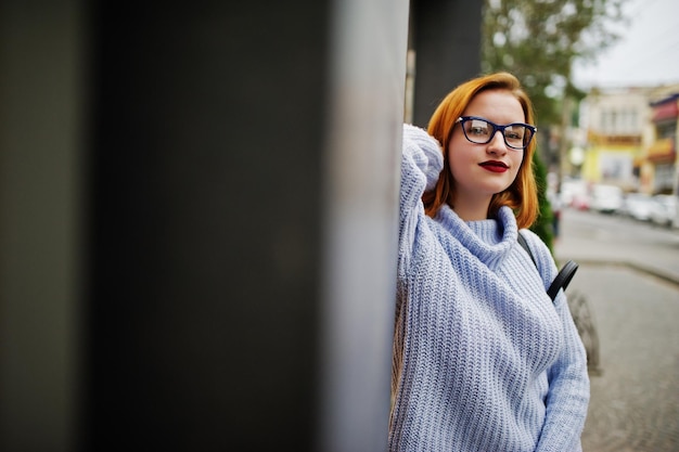 Alegre e linda mulher ruiva em óculos quente suéter de lã azul com mochila posada ao ar livre