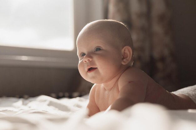 Alegre e sorridente bebê recém-nascido em uma fralda está de bruços em uma cama branca feliz infância despreocupada