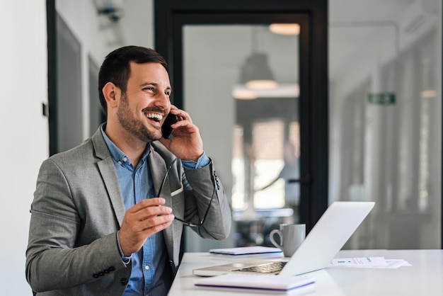 Alegre empresário falando no celular enquanto trabalhava no laptop no escritório