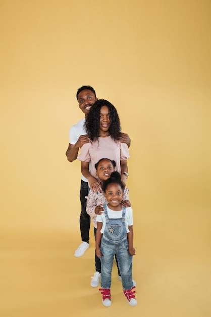 Foto alegre familia afroamericana de cuatro parados uno detrás del otro y sonriendo a la cámara