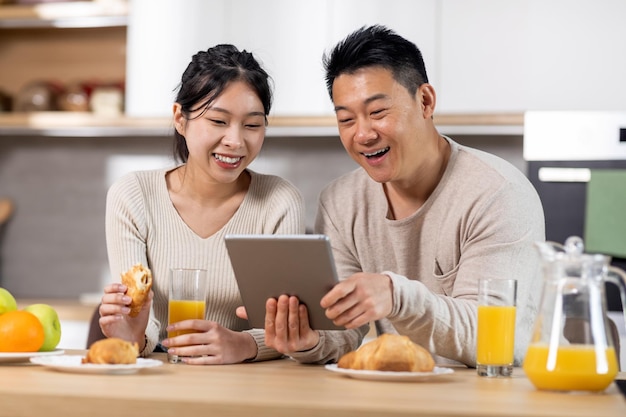 Alegre família asiática usando tablet digital enquanto toma café da manhã