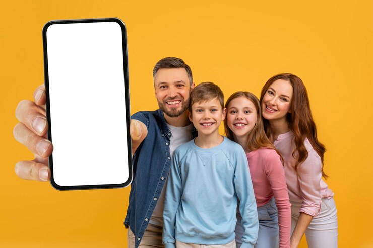 Una alegre familia de cuatro personas está posando estrechamente juntos con el padre extendiendo su brazo para mostrar un