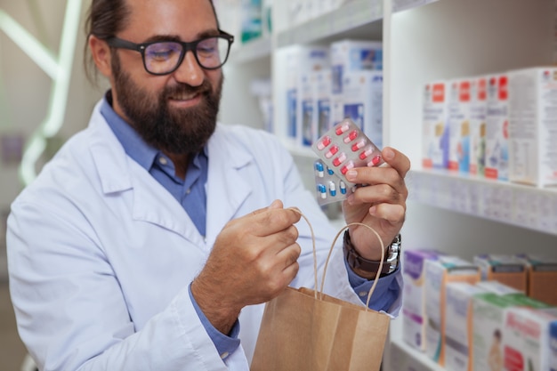 Alegre farmacéutico vendiendo medicamentos en su farmacia