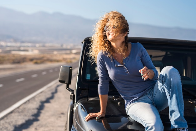 Foto alegre feliz, senhora sentada no carro em viagens aventura férias sorria e desfrute da liberdade - motorista e veículo com a estrada no fundo - conceito de pessoas alegres e solteiras de estilo de vida