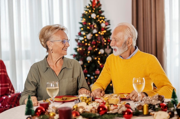 Una alegre y festiva pareja de ancianos está sentada en la mesa del comedor en una casa acogedora en Navidad y Año Nuevo