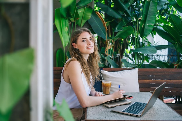 Alegre freelancer feminina tomando notas perto de plantas tropicais