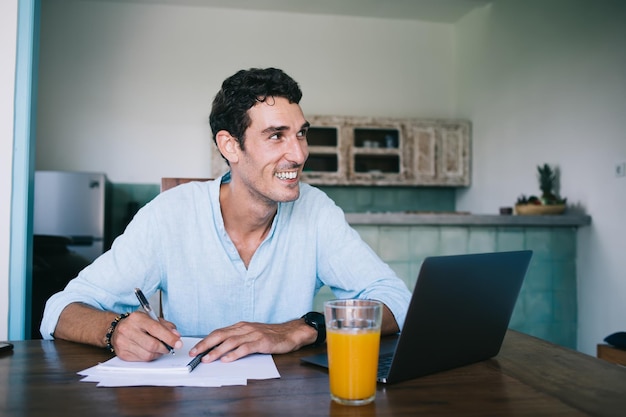 Alegre freelancer masculino fazendo anotações de negócios na mesa