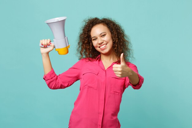 Alegre garota africana em roupas casuais, segurando o megafone na mão aparecendo o polegar isolado no fundo da parede azul turquesa no estúdio. Conceito de estilo de vida de emoções sinceras de pessoas. Simule o espaço da cópia.