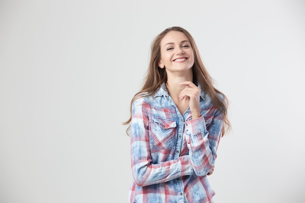 Alegre garota vestida com uma camisa quadriculada sorri em pé sobre o fundo branco no estúdio.