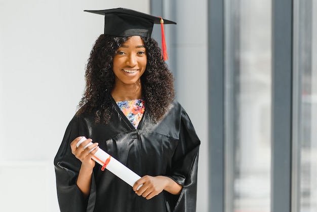 Alegre graduada afroamericana de pie frente al edificio de la universidad