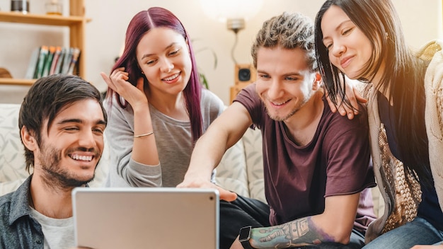 Alegre grupo de amigos divirtiéndose en casa mientras usa una tableta digital