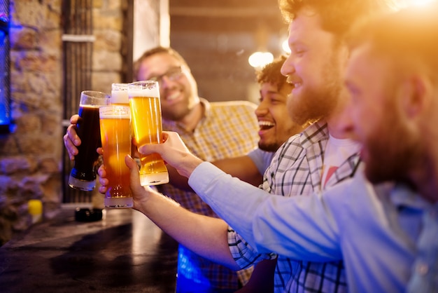 Foto alegre grupo de amigos comemorando com chope no bar. foco vista sobre os copos de cerveja.