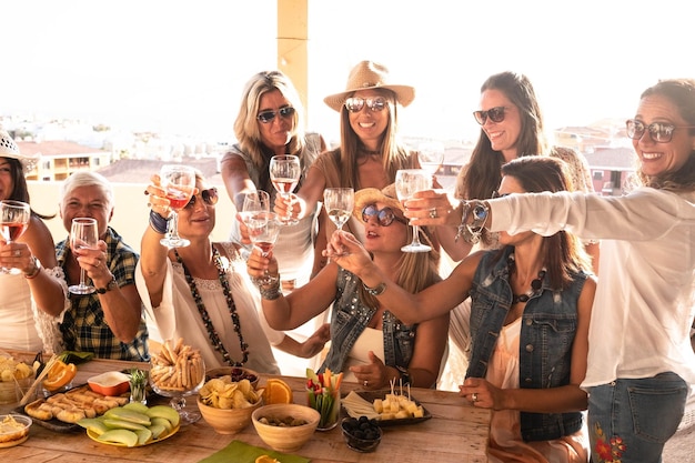 Alegre grupo de mulheres comemorando férias no campo do terraço Amigos sorrindo e desfrutando de aperitivo com comida e bebida Céu claro no fundo