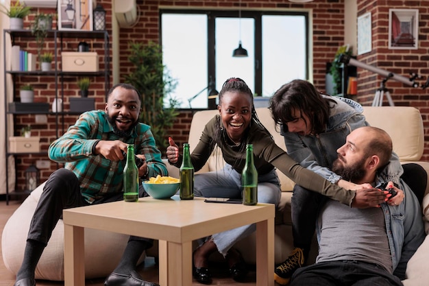 Alegre grupo de pessoas se divertindo com a estratégia de videogames, jogando competição no console de tv e bebendo cerveja. Jovens curtindo festa em casa juntos, atividade de lazer.