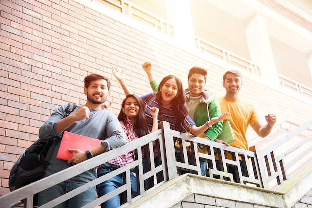 Alegre grupo de jóvenes asiáticos indios de estudiantes universitarios o amigos caminando en el pasillo del campus o en las escaleras