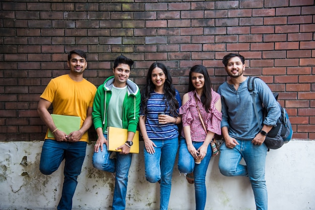 Alegre grupo de jóvenes asiáticos indios de estudiantes universitarios o amigos riendo juntos mientras están sentados, de pie o caminando en el campus