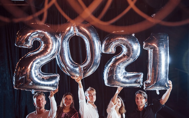 Alegre grupo de personas con bebidas y globos en las manos celebrando el nuevo año 2021.