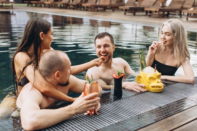 Alegre grupo positivo de amigos relajándose y nadando en la piscina en verano