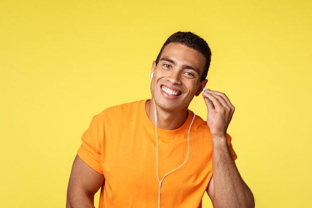 Alegre guapo atleta masculino en camiseta naranja coloca auriculares en el oído y sonríe