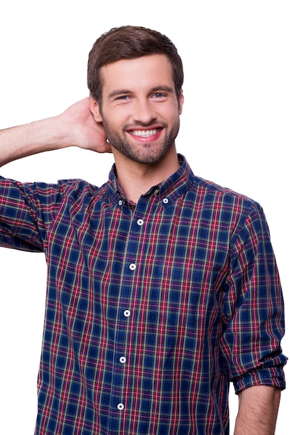 Alegre guapo. Retrato de joven guapo en camisa casual sosteniendo la mano detrás de la cabeza y sonriendo mientras está de pie aislado en blanco