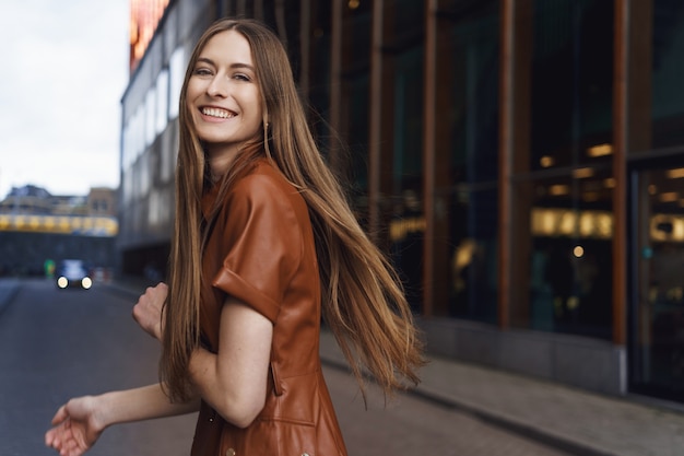 Alegre hermosa joven se da la vuelta para sonreír y mirar a la cámara mientras camina por las calles de la ciudad.