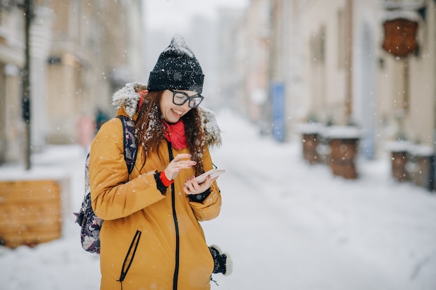 Alegre hermosa morena de moda de invierno con smartphone en calle urbana