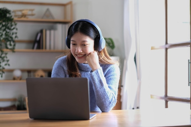 Alegre y hermosa mujer asiática con auriculares y mirando a la tableta digital en una reunión de videollamadas y estudiando en línea en Internet