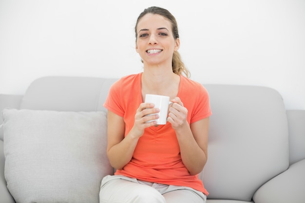 Alegre hermosa mujer sosteniendo una taza sentada en el sofá