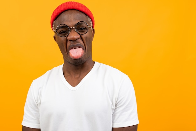 Alegre hombre americano negro en camiseta blanca burlas mostrando lengua en amarillo con espacio de copia