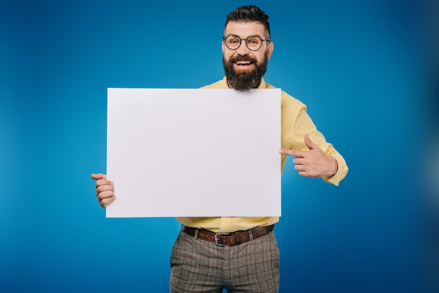 Alegre hombre barbudo apuntando al tablero vacío aislado en azul