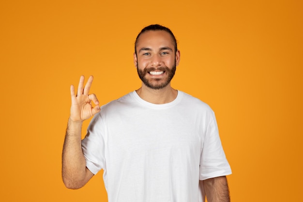 Alegre hombre europeo adulto con barba en camiseta blanca haciendo el signo correcto con la mano