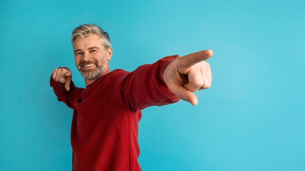 Alegre hombre de mediana edad apuntando al espacio de copia en azul