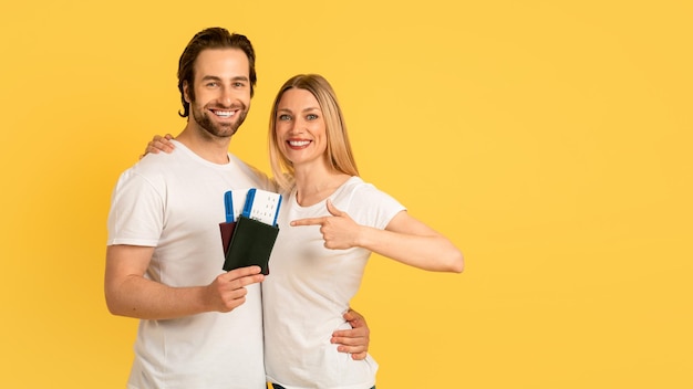 Alegre hombre y mujer caucásicos milenarios con camisetas blancas señalan con el dedo los pasaportes con aire