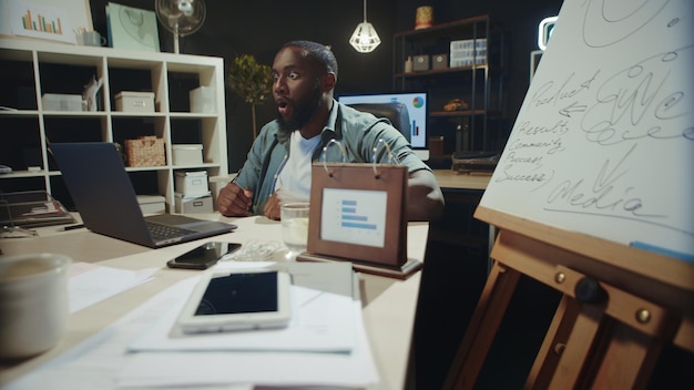 Alegre hombre de negocios afroamericano leyendo excitantes noticias en línea en coworking Un emocionado hombre afro celebrando el éxito en una oficina hipster Un hombre africano satisfecho levantando las cejas emocionalmente en el interior