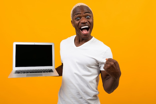Alegre hombre negro americano con una hermosa sonrisa blanca como la nieve en una camiseta blanca con una computadora portátil con un diseño en naranja