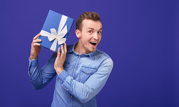 Alegre hombre sorprendido con cabello oscuro escucha lo que traquetea en un regalo.