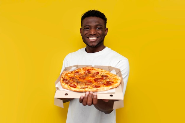 Alegre homem afro-americano em camiseta branca segura caixa de pizza e sorri em fundo amarelo