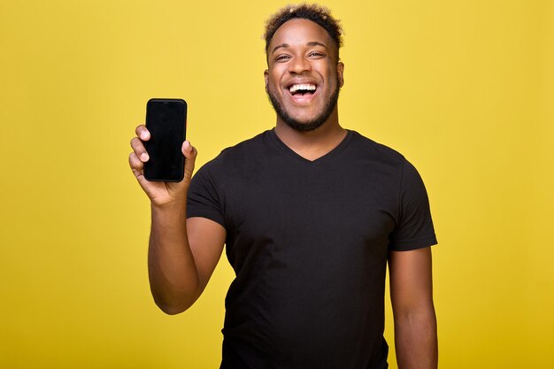 Alegre homem afro-americano segura o celular na mão sobre fundo amarelo