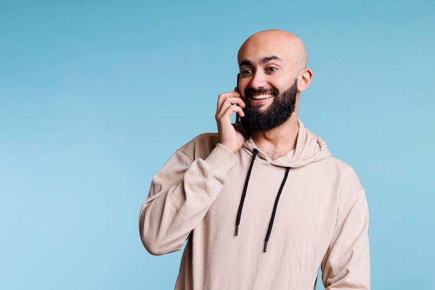 Alegre homem árabe tendo conversa divertida no smartphone e sorrindo enquanto fala. Pessoa conversando no celular e ouvindo o interlocutor com expressão facial alegre e animada