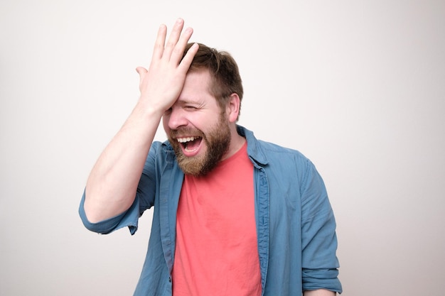 Alegre homem barbudo rindo feliz por ter lembrado de algo importante que ele segura a mão na testa