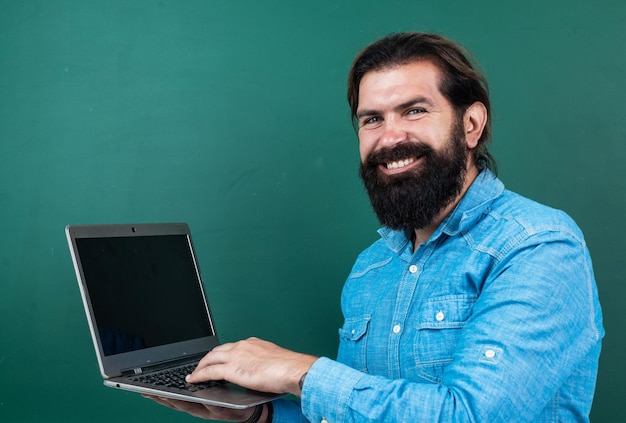 Alegre homem bem sucedido e confiante com barba trabalhando em tecnologia online de laptop