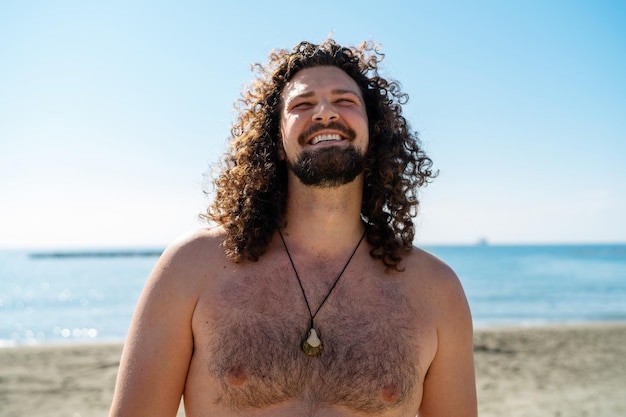 Alegre homem encaracolado relaxando na praia durante o dia ensolarado de verão